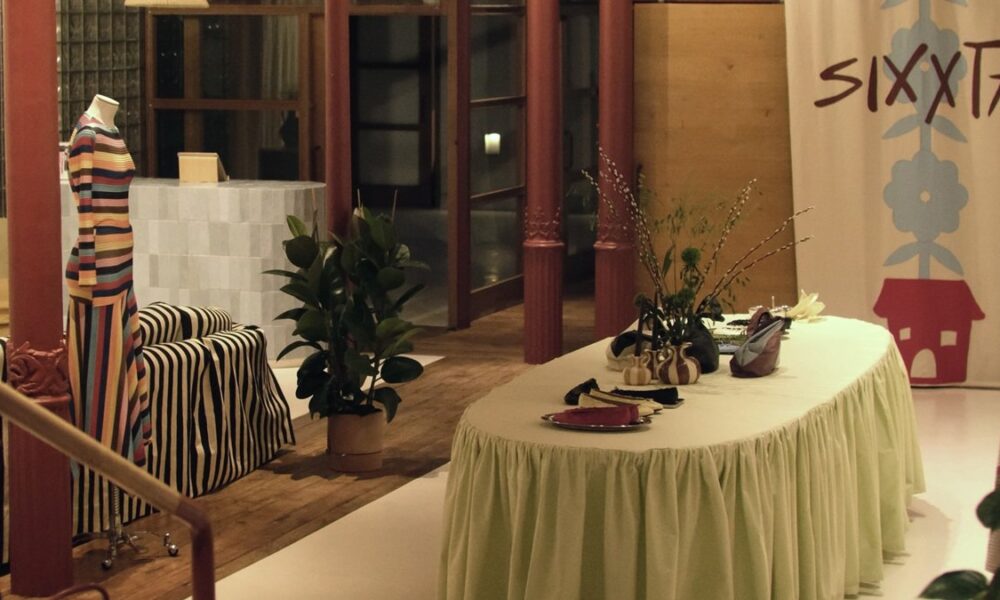 Maniquí con vestido de rayas, junto a sofá , planta y mesa con floreros, Al fondo entrada a la tienda