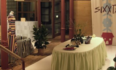 Maniquí con vestido de rayas, junto a sofá , planta y mesa con floreros, Al fondo entrada a la tienda